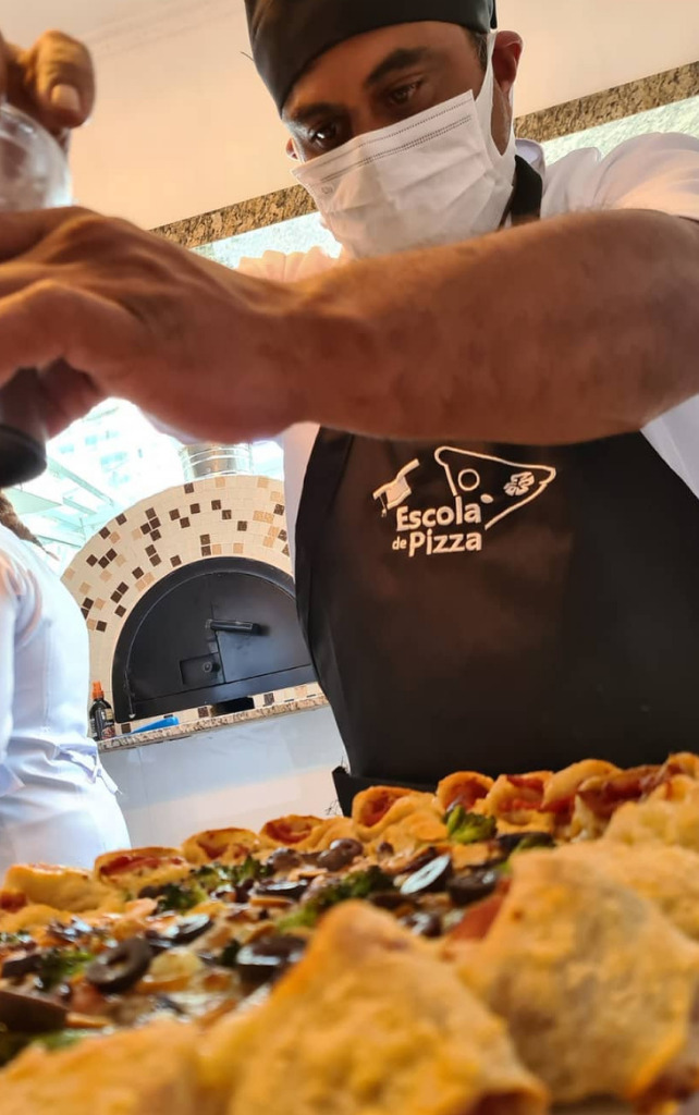 homem tempera a pizza com recheios que ele mesmo fez