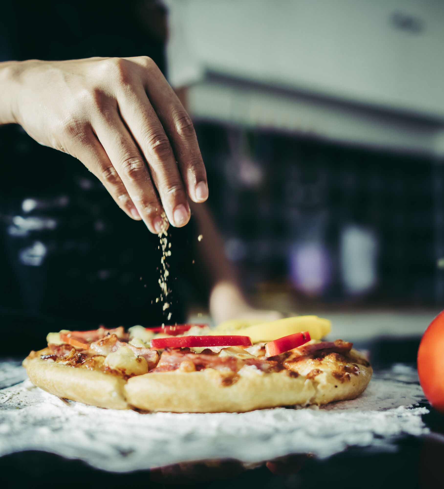 Close up of woman hand putting oregano over tomato and mozzarella on a pizza. Cooking concept